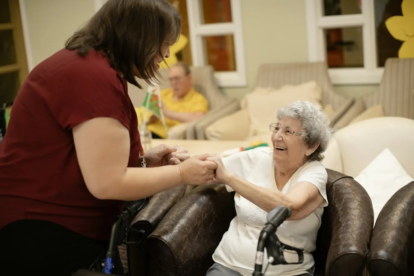A support worker holding hands with a smiling older woman who is seated