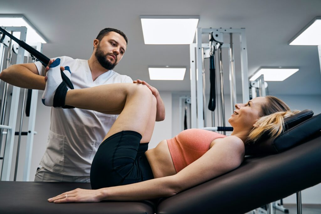 Physical therapist assisting a female patient with a leg exercise in a clinic.